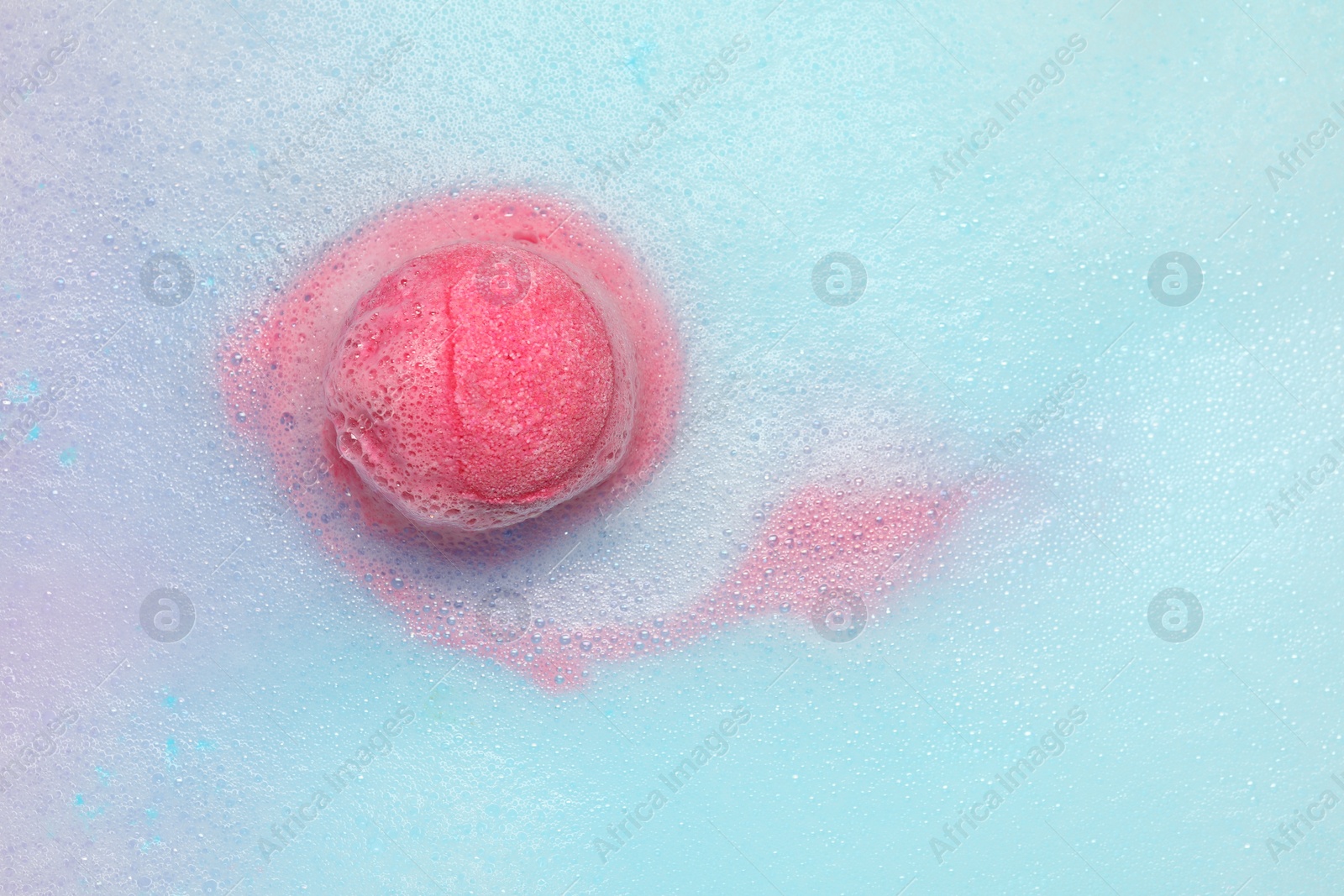 Photo of Pink bath bomb dissolving in water. Space for text