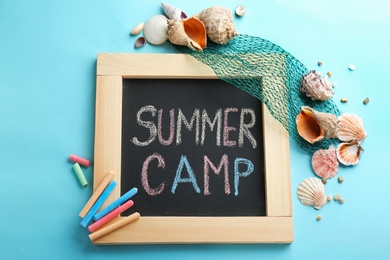 Text "SUMMER CAMP" on small blackboard, colorful chalk and shells, top view