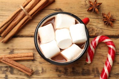 Photo of Tasty hot chocolate with marshmallows, candy cane and spices on wooden table, flat lay