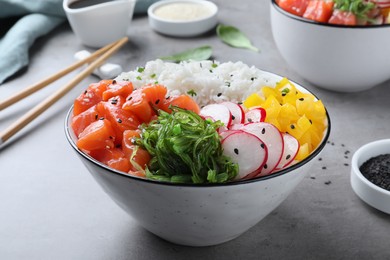 Delicious poke bowl with salmon and vegetables served on light grey table, closeup