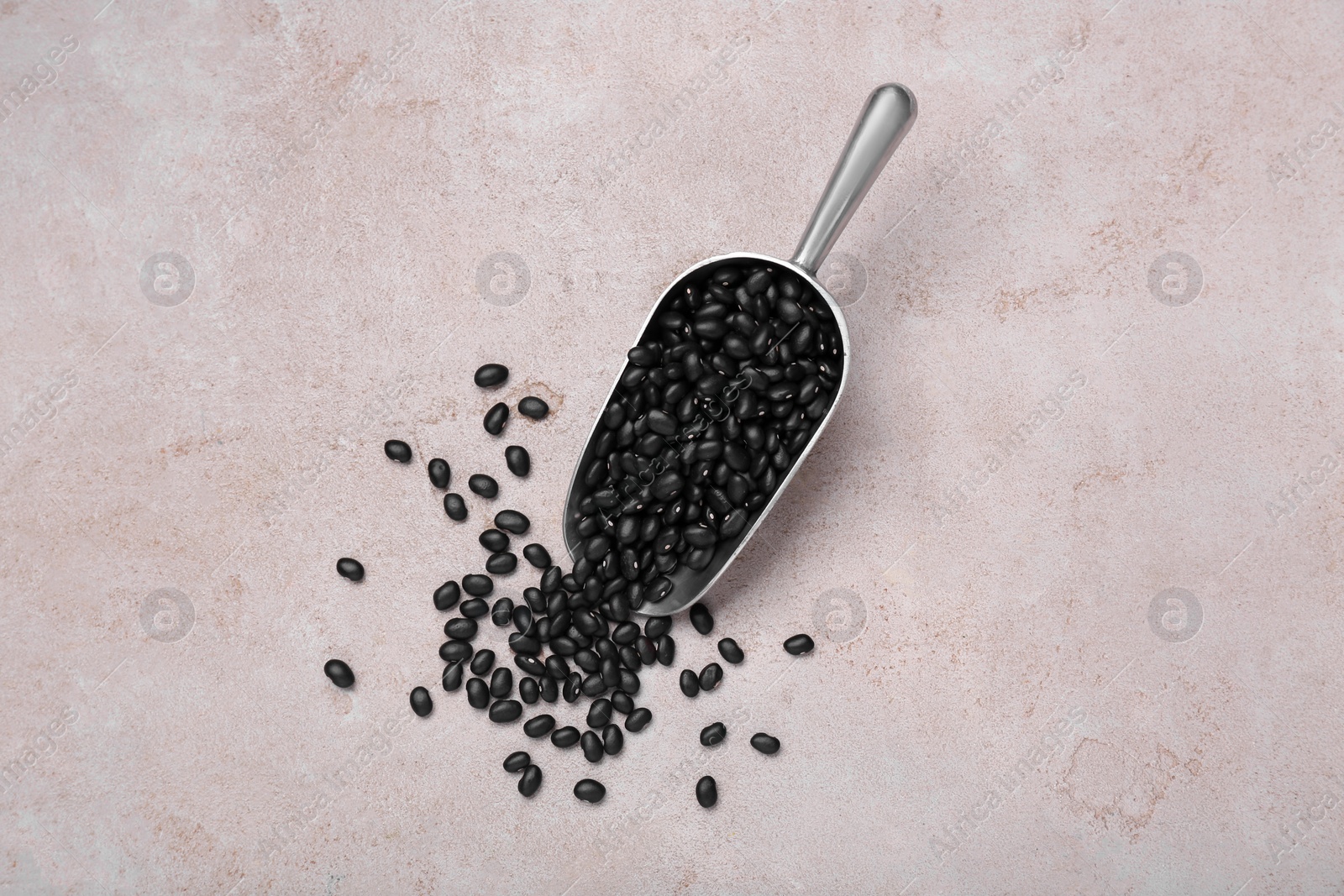 Photo of Scoop of raw black beans on light grey table, top view