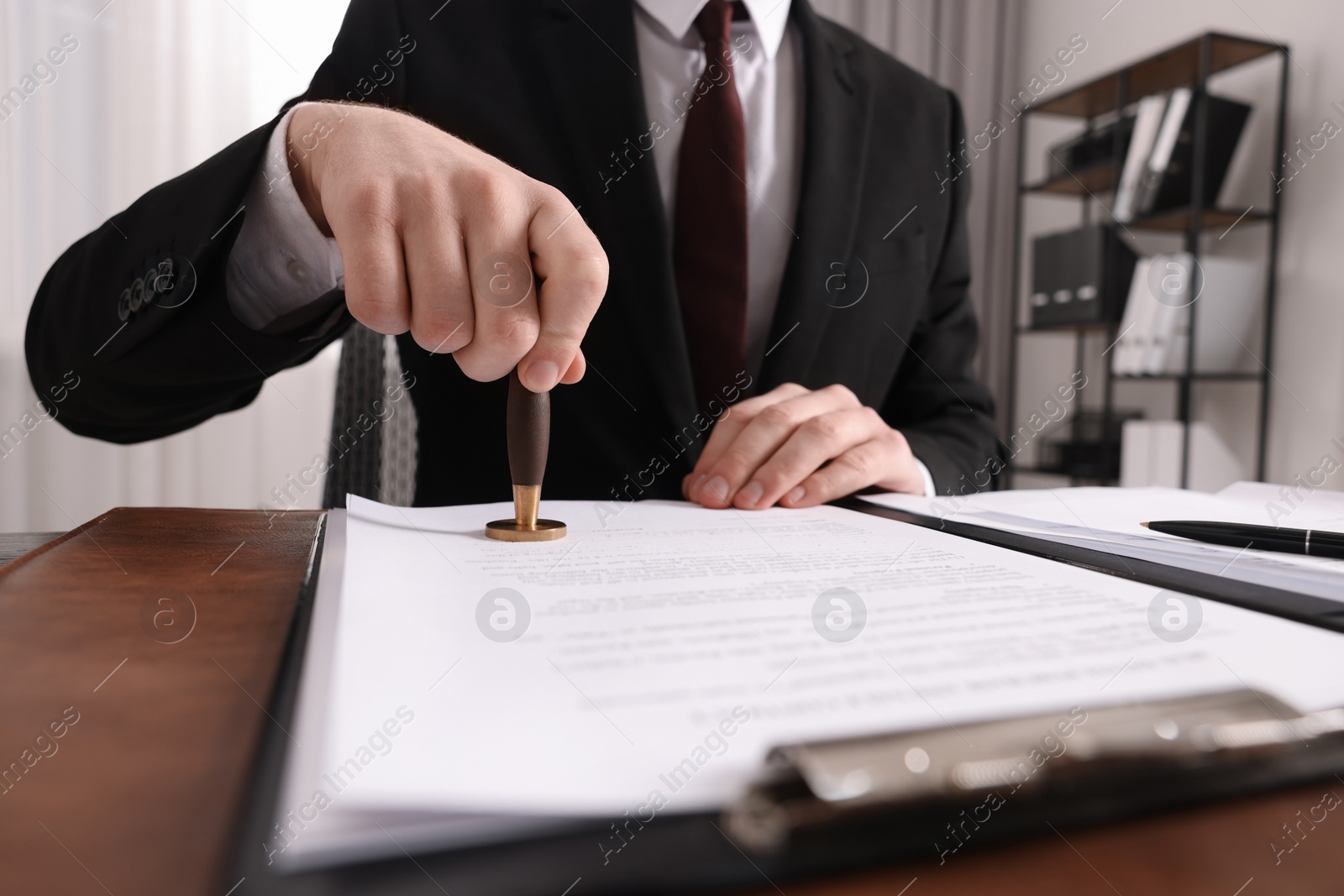 Photo of Notary stamping document at wooden table in office, closeup