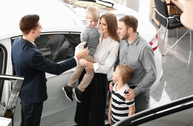 Photo of Salesman giving car key to young family in salon