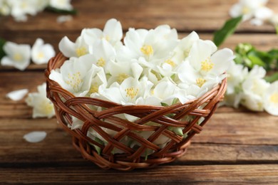 Photo of Beautiful jasmine flowers in wicker bowl on wooden table, closeup
