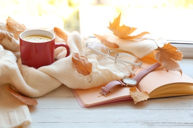 Composition with cup of hot drink, sweater and autumn leaves on windowsill. Cozy atmosphere