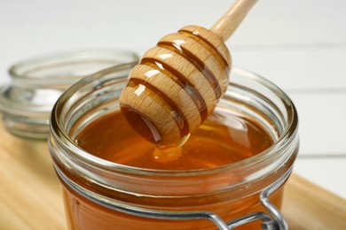 Photo of Pouring honey from dipper into jar at table, closeup