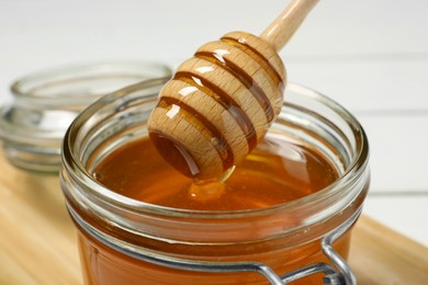 Pouring honey from dipper into jar at table, closeup