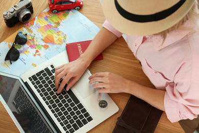 Photo of Woman using laptop to plan trip at wooden table, closeup