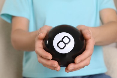 Woman holding magic eight ball indoors, closeup