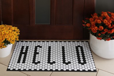 Photo of Stylish door mat with word HELLO and beautiful flowers on floor