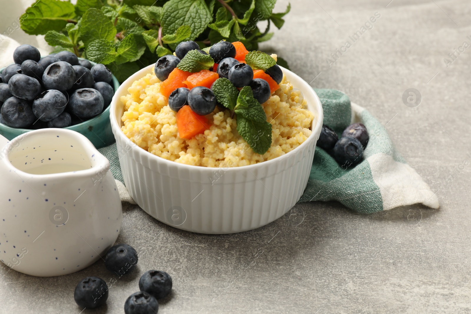 Photo of Tasty millet porridge with blueberries, pumpkin and mint in bowl on light grey table