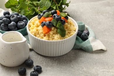 Tasty millet porridge with blueberries, pumpkin and mint in bowl on light grey table