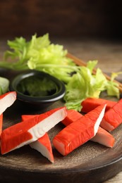 Photo of Fresh crab sticks with lettuce and soy sauce on wooden plate, closeup