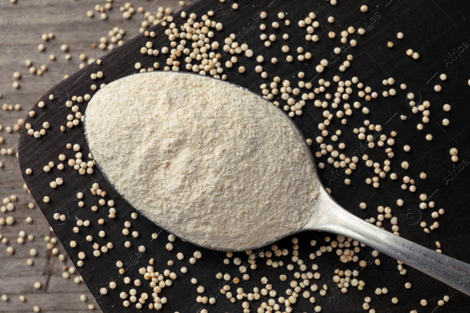 Photo of Spoon with quinoa flour and seeds on black wooden table, closeup