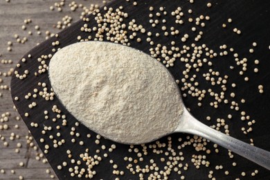 Spoon with quinoa flour and seeds on black wooden table, closeup