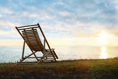 Photo of Empty wooden deckchair on hill near calm river