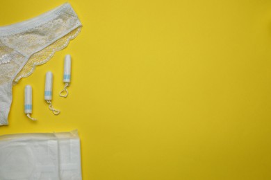 Photo of Woman's panties, menstrual pads and tampons on yellow background, flat lay. Space for text