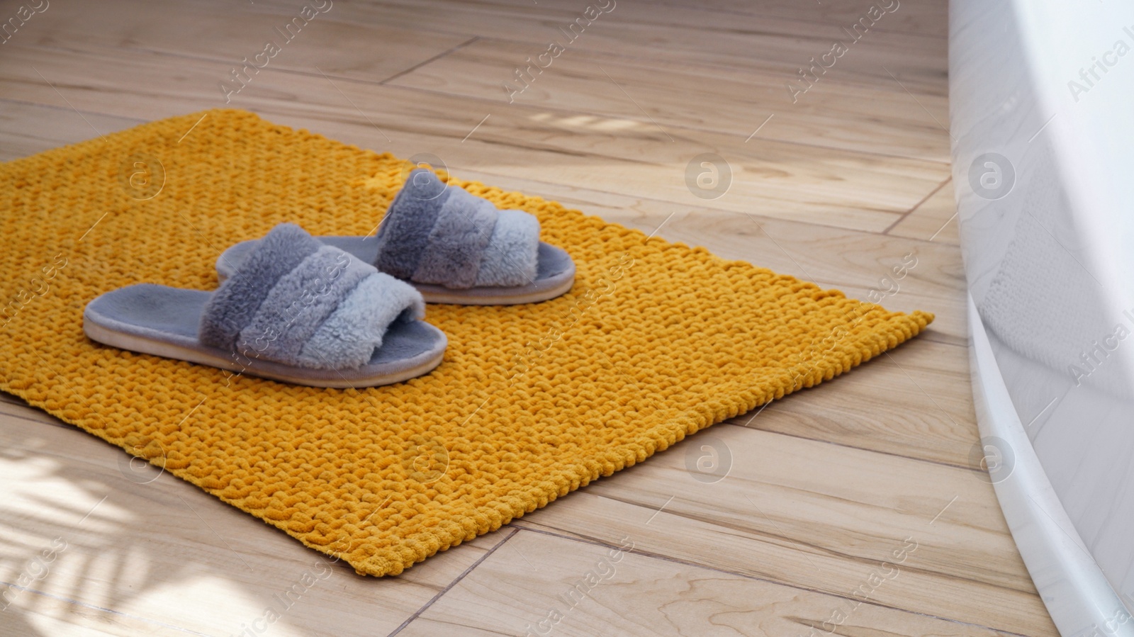 Photo of Soft bath mat with slippers near tub on wooden floor in bathroom