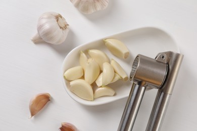 Photo of Metal press and garlic on white wooden table, flat lay