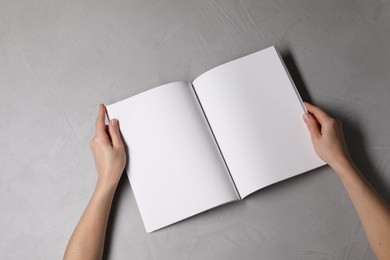 Photo of Woman holding open notebook with blank pages at light grey table, top view. Mockup for design