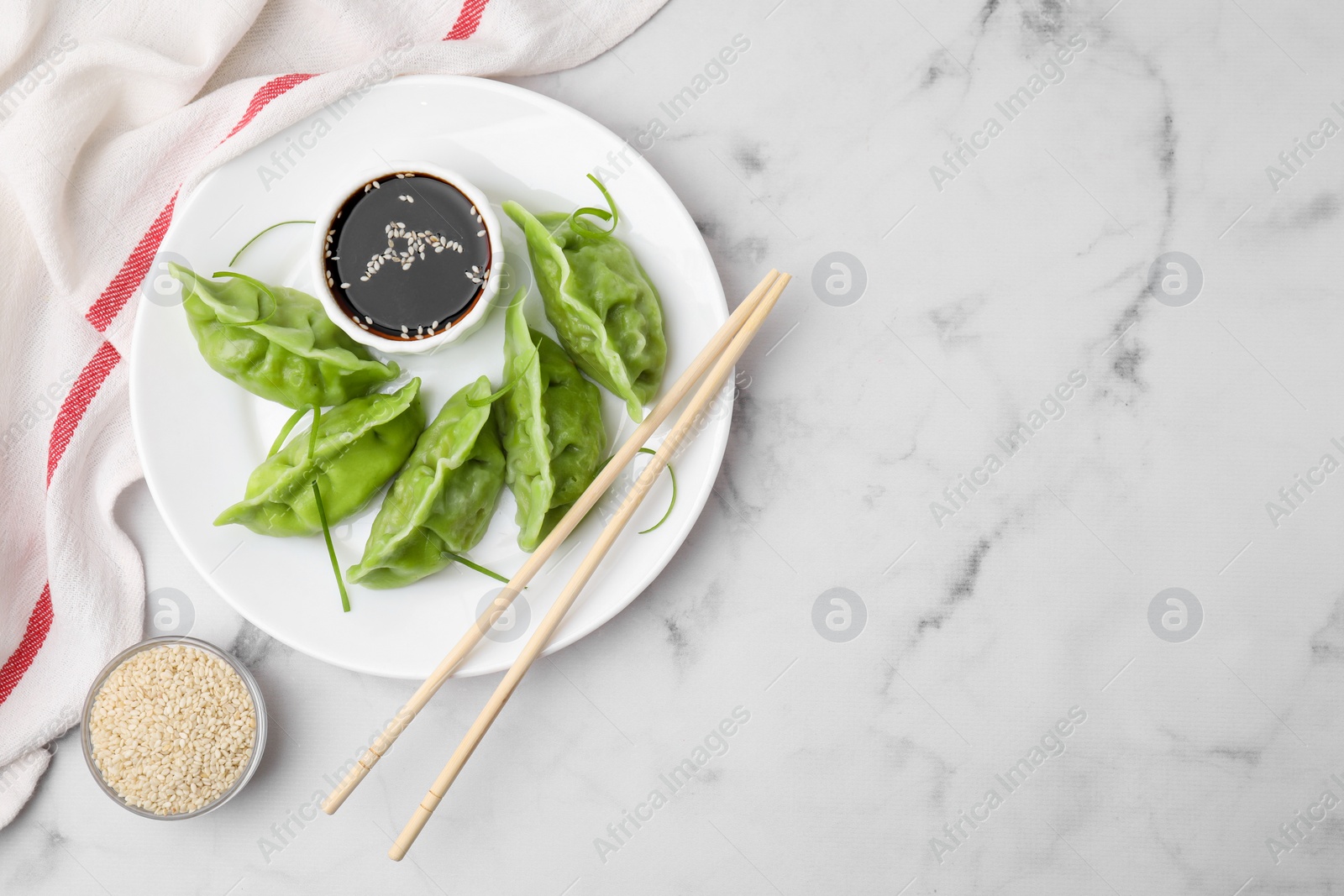 Photo of Delicious green dumplings (gyozas) and soy sauce served on white marble table, flat lay. Space for text