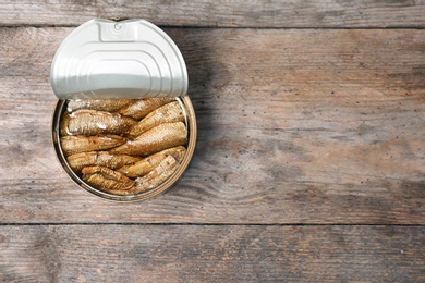 Photo of Tin can with conserved fish on wooden background, top view