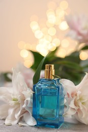 Photo of Bottle of perfume and beautiful lily flowers on table against beige background with blurred lights, closeup