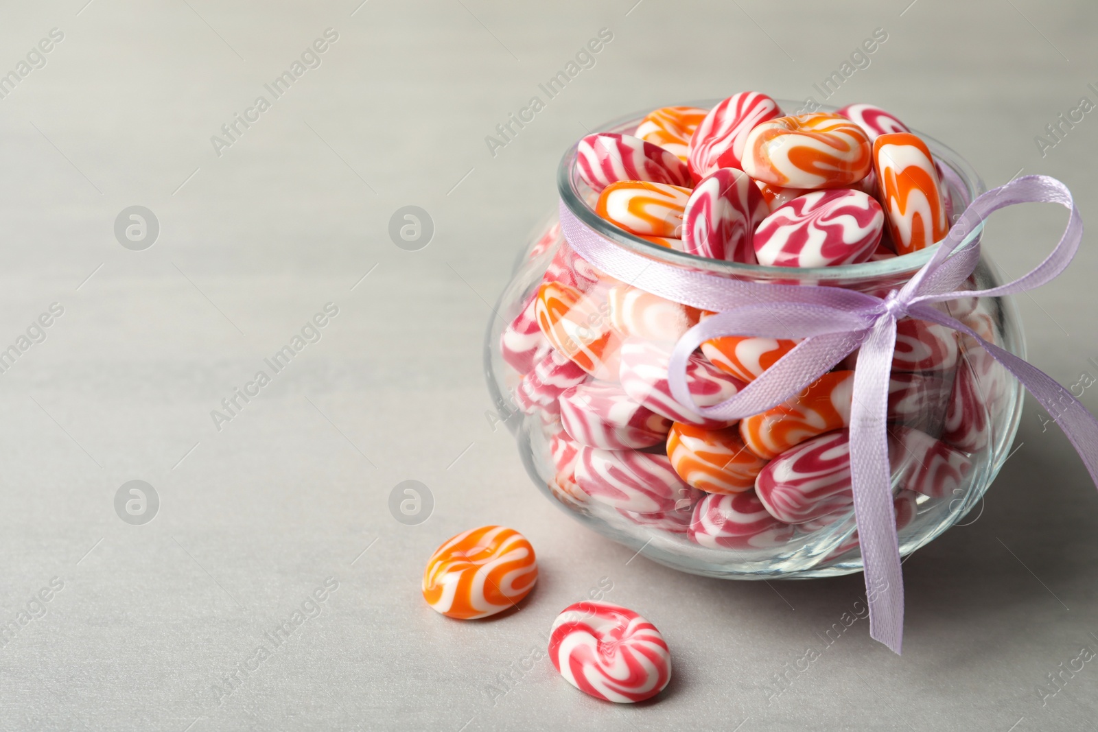 Photo of Sweet candies in glass jar on light grey table. Space for text