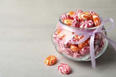 Photo of Sweet candies in glass jar on light grey table. Space for text