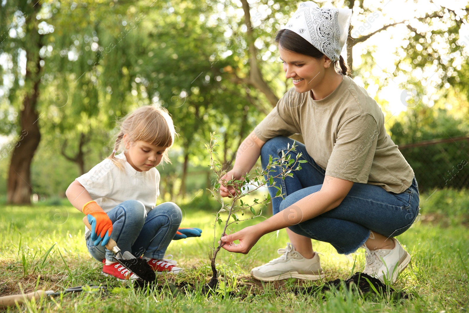 Photo of Mother and her daughter planting tree together in garden