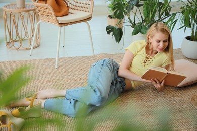 Photo of Happy young woman reading book on floor at indoor terrace