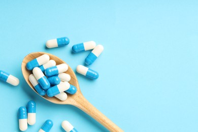 Photo of Many antibiotic pills with wooden spoon and space for text on light blue background, top view. Medicinal treatment