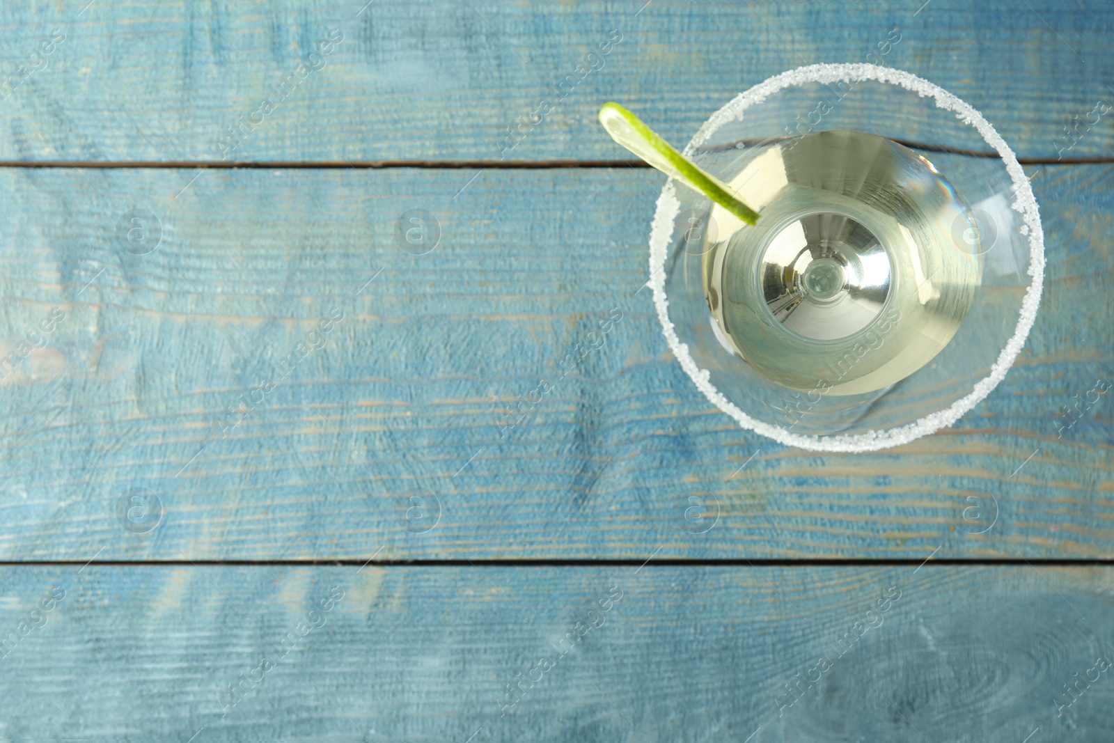 Photo of Glass of Lime Drop Martini cocktail on light blue wooden table, top view. Space for text