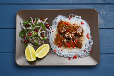 Photo of Pieces of soy sauce chicken with noodle, salad and lime on blue wooden table, top view