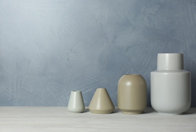 Photo of Beautiful ceramic vases on table against color wall. Space for text