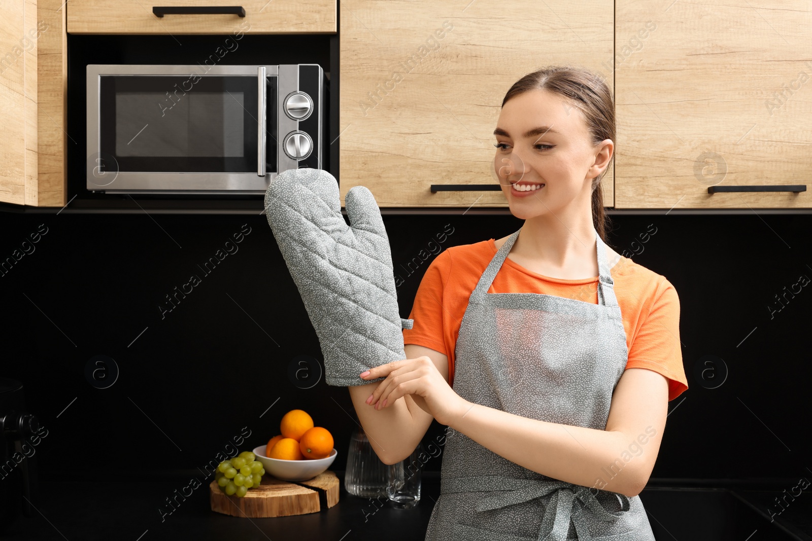 Photo of Beautiful young woman in clean apron and oven glove at kitchen