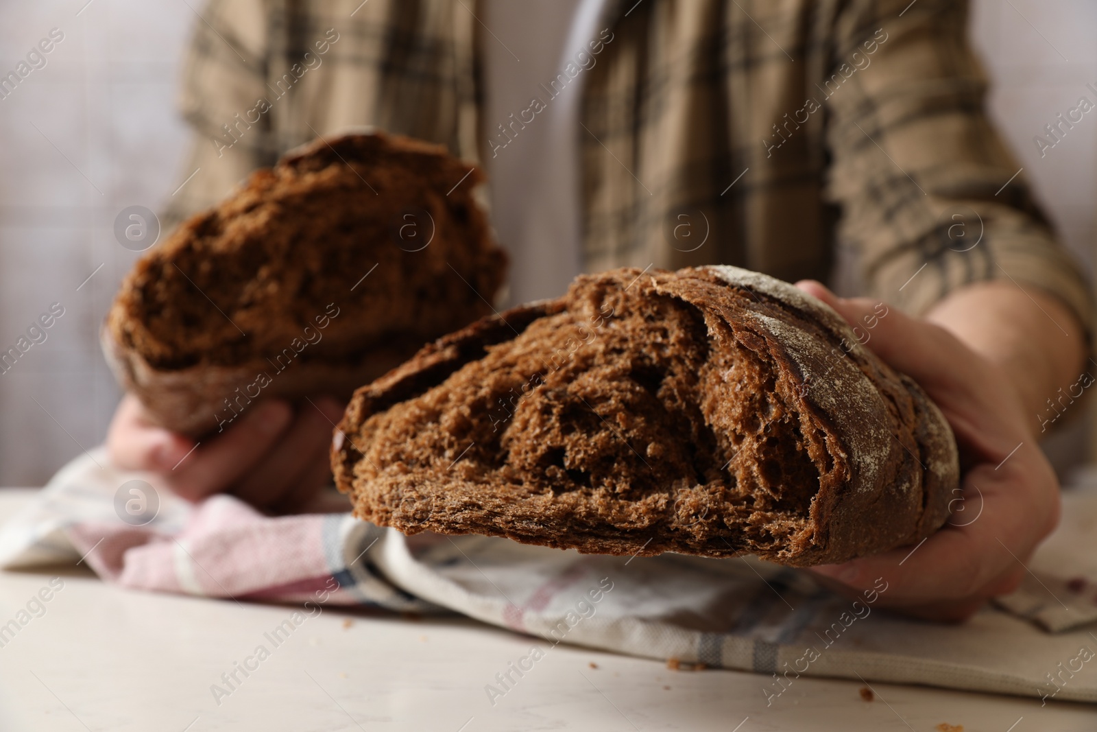 Photo of Man holding loaf of fresh broken bread on white table, closeup