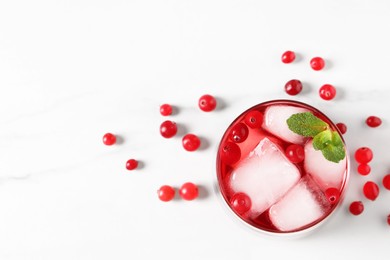 Tasty cranberry juice with ice cubes in glass and fresh berries on white wooden table, top view. Space for text