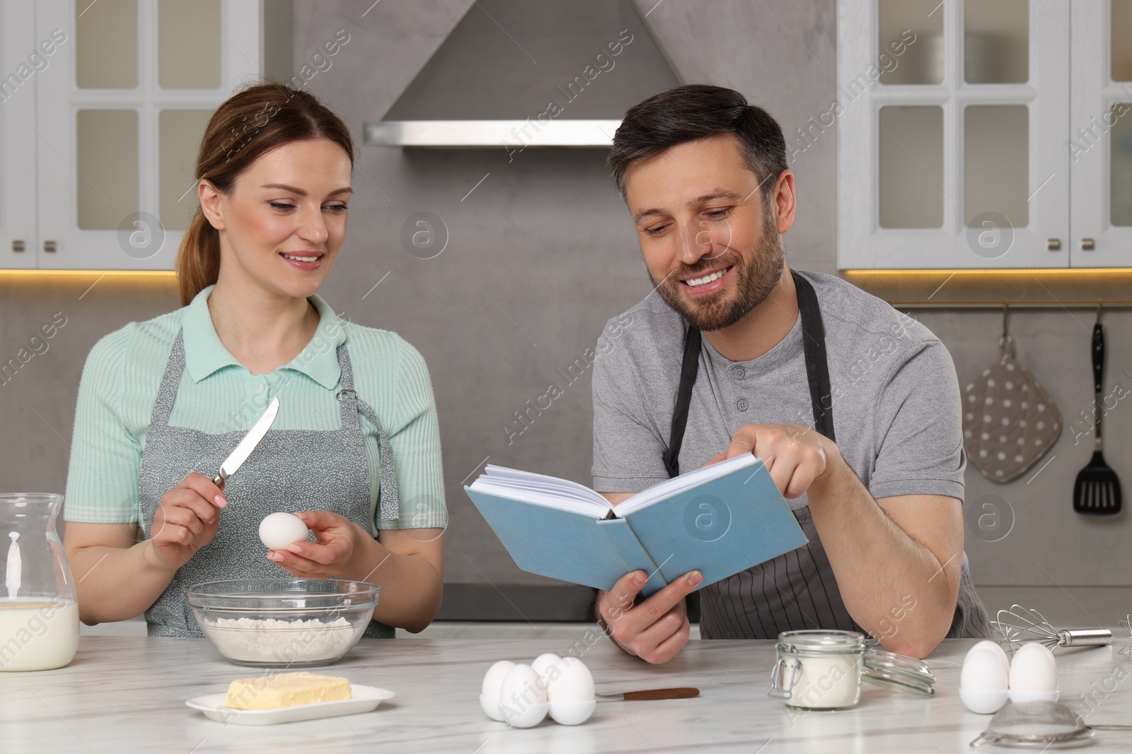 Photo of Happy couple cooking by recipe book in kitchen