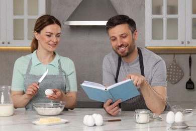 Happy couple cooking by recipe book in kitchen