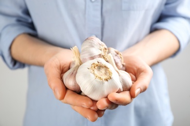 Photo of Woman holding pile of garlic bulbs on light background, closeup. Natural antibiotic