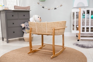 Photo of Beautiful cradle with toy rabbit near crib and dresser in baby room. Interior design