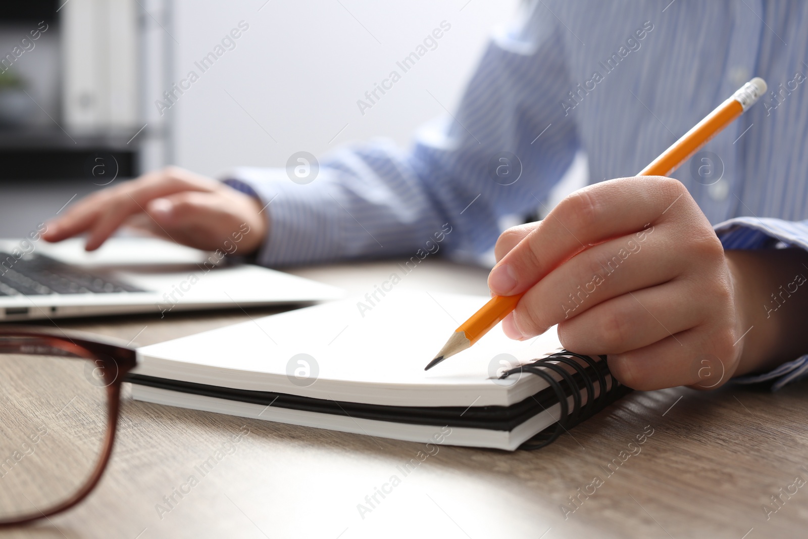 Photo of Woman with notebook working on laptop at wooden table in office, closeup