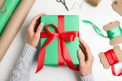 Woman wrapping Christmas gift at white wooden table, top view