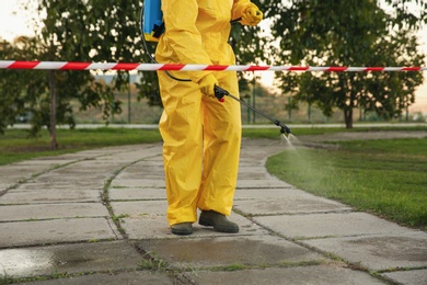 Photo of Person in hazmat suit disinfecting street pavement with sprayer, closeup. Surface treatment during coronavirus pandemic
