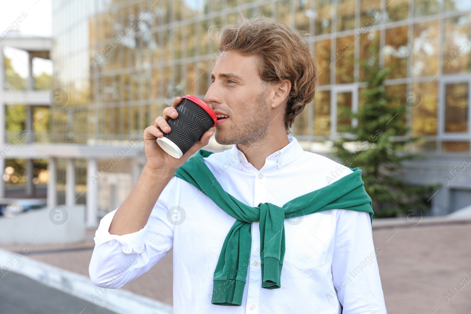 Photo of Portrait of handsome young man with cup of coffee on city street