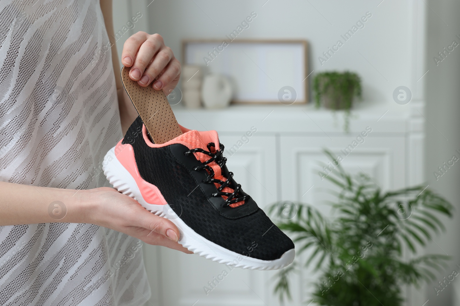 Photo of Woman putting orthopedic insole into shoe indoors, closeup. Foot care