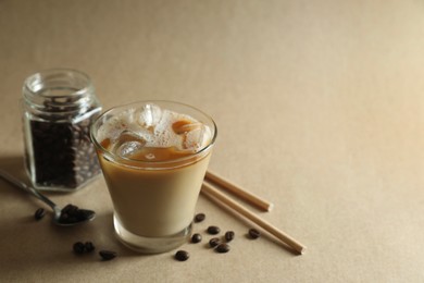 Photo of Refreshing iced coffee with milk in glass, straws and beans on beige background, closeup. Space for text