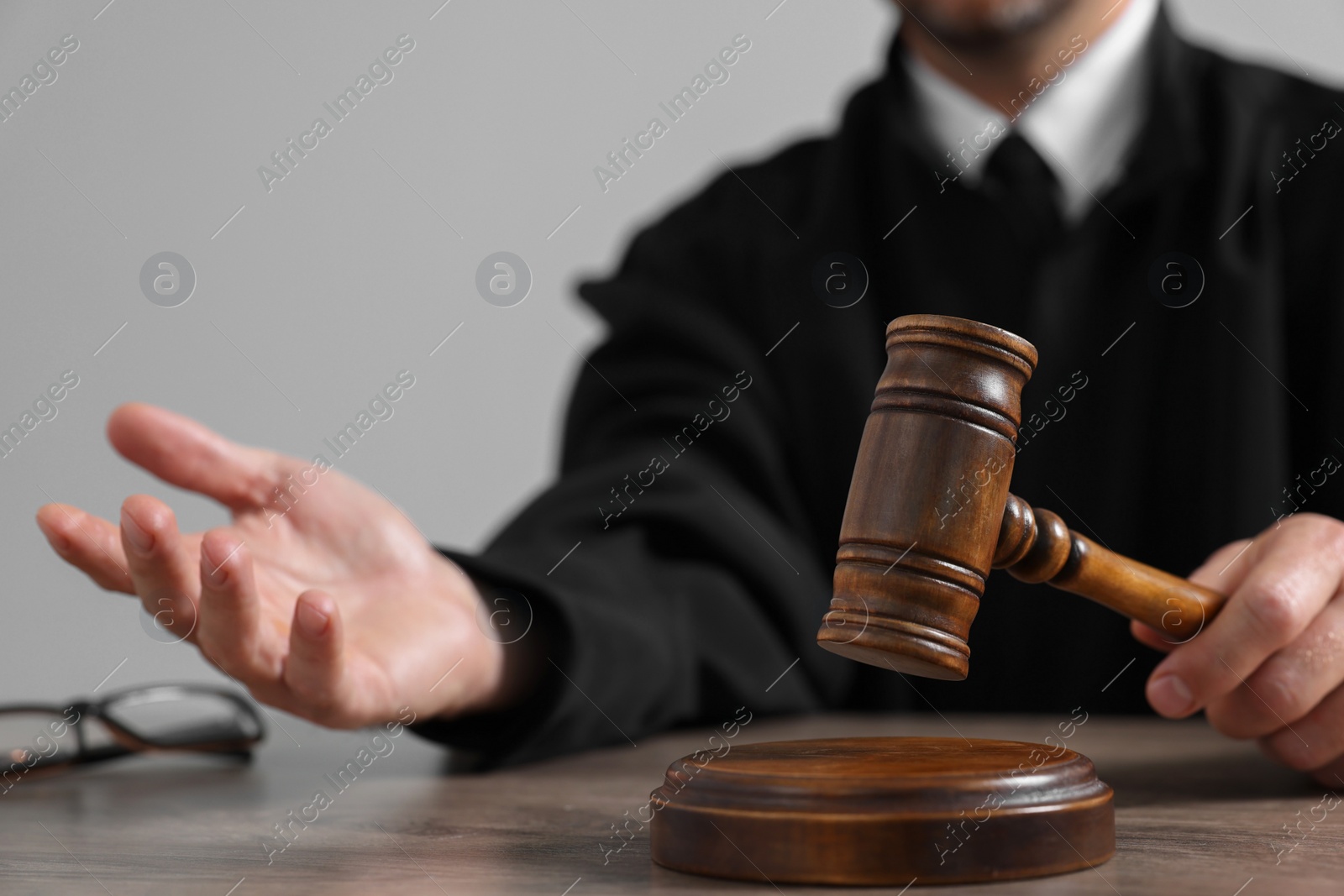 Photo of Judge with gavel sitting at wooden table against light grey background, closeup