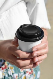 Woman holding takeaway coffee cup outdoors, closeup